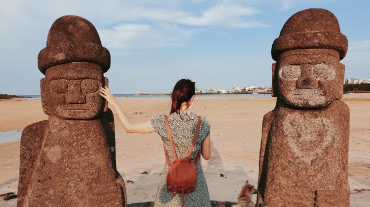 Sur une plage de l'ile de Jeju en Corée du Sud, je me tiens de dos entre deux statues en pierre typiques de l'ile.